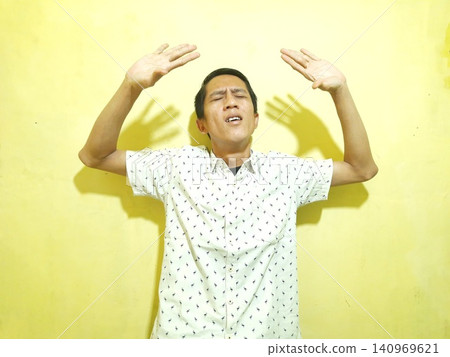 Young Asian Man Feeling Stressed with Headache Against Yellow Wall 140969621