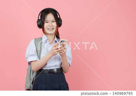 Student in uniform listening music from Smartphone with Headphone studio isolated pink background. Student in uniform listening music from Smartphone with Headphone studio isolated pink background. 140969795