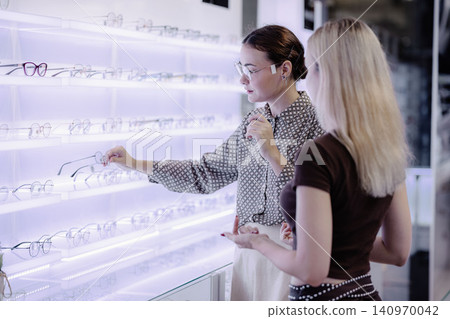 Young woman trying on eyeglasses in optical store, happy customer shopping for new eyewear Young woman trying on eyeglasses in optical store, happy customer shopping for new eyewear 140970042