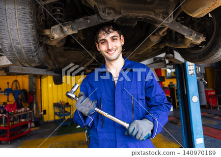 Happy garage male worker standing smile work service under car maintenance steering wheel suspension Happy garage male worker standing smile work service under car maintenance steering wheel suspension 140970189