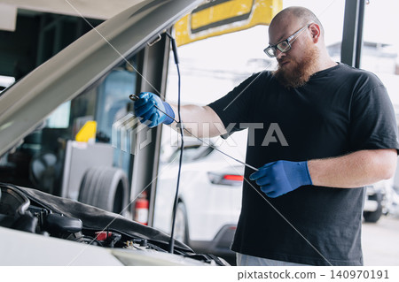 Garage Mechanic worker in auto service center working check and change engine oil under hood. Garage Mechanic worker in auto service center working check and change engine oil under hood. 140970191