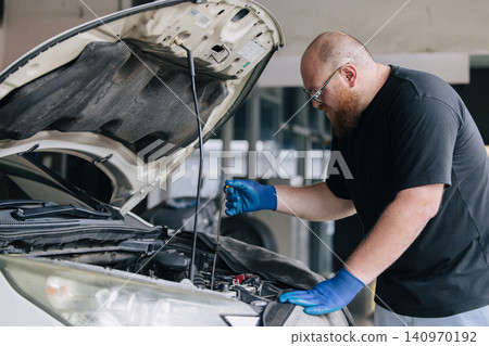 Garage Mechanic worker in auto service center working check and change engine oil under hood. Garage Mechanic worker in auto service center working check and change engine oil under hood. 140970192