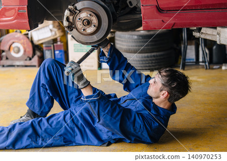 Garage Mechanic worker in auto service center working steering brake service maintenance under car. Garage Mechanic worker in auto service center working steering brake service maintenance under car. 140970253
