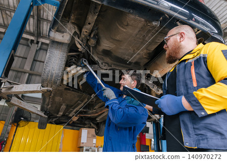 Garage Mechanic worker in auto service center working steering brake service maintenance under car. Garage Mechanic worker in auto service center working steering brake service maintenance under car. 140970272