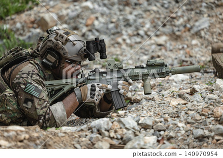 Military sniper aiming precision rifle during tactical reconnaissance mission in rocky terrain Military sniper aiming precision rifle during tactical reconnaissance mission in rocky terrain 140970954