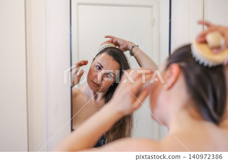 A woman gently combs her hair as part of her daily beauty care routine, promoting healthy, smooth, and well-groomed locks. A woman gently combs her hair as part of her daily beauty care routine, promoting healthy, smooth, and well-groomed locks. 140972386