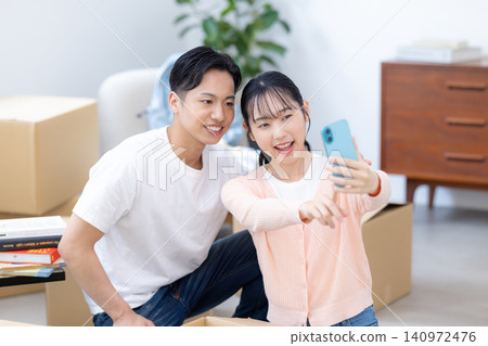 一對夫婦在搬家過程中一邊整理行李一邊用智慧型手機自拍。 一對夫婦在搬家過程中一邊整理行李一邊用智慧型手機自拍。 140972476