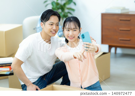 A couple takes selfies with their smartphones while unpacking during a move. A couple takes selfies with their smartphones while unpacking during a move. 140972477