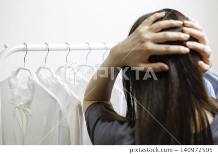 一位女士背對著鏡頭,凝視著衣架上整齊排列的衣服,陷入沉思。 一位女士背對著鏡頭,凝視著衣架上整齊排列的衣服,陷入沉思。 140972505