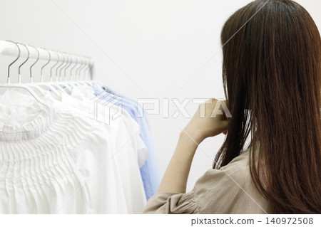 The back view of a woman looking at clothes lined up on a hanger rack, deep in thought. The back view of a woman looking at clothes lined up on a hanger rack, deep in thought. 140972508