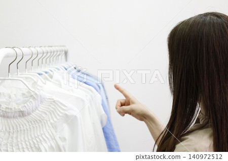 一位女士指著掛在衣架上的衣服。 140972512