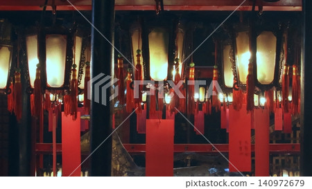 Lit hanging lamps decorated in auspicious red ribbons and red tags for the Chinese New Year in Man Mo Temple. Sheung Wan, Hong Kong Lit hanging lamps decorated in auspicious red ribbons and red tags for the Chinese New Year in Man Mo Temple. Sheung Wan, Hong Kong 140972679