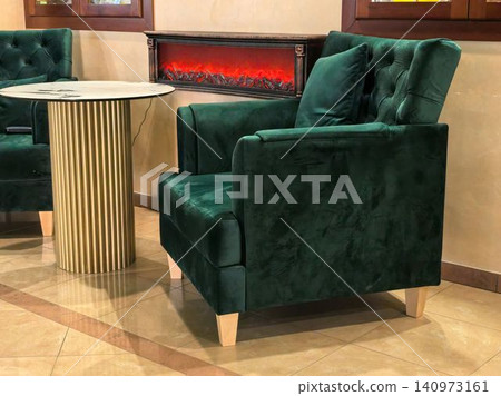 Dark green velvet tufted armchair beside electric fireplace and gold table Dark green velvet tufted armchair beside electric fireplace and gold table 140973161