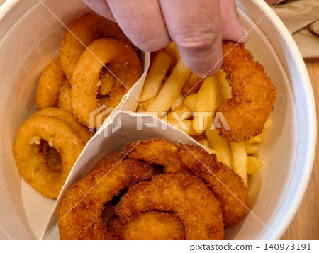 Hand picking crispy onion ring from bowl with fries Hand picking crispy onion ring from bowl with fries 140973191