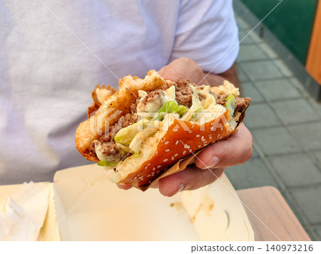 Man holding a bitten sesame burger outdoors at a cafe terrace Man holding a bitten sesame burger outdoors at a cafe terrace 140973216