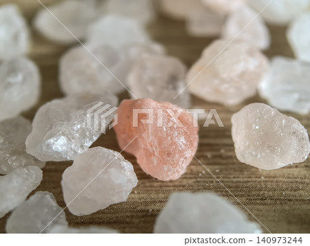 Pink Himalayan salt crystal among white rock salt crystals on wooden surface Pink Himalayan salt crystal among white rock salt crystals on wooden surface 140973244