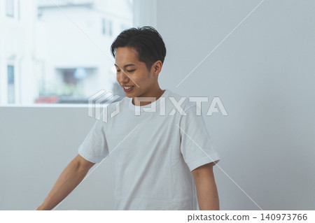 A refreshing portrait of a man with a broad smile, looking down in a white room. A refreshing portrait of a man with a broad smile, looking down in a white room. 140973766