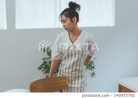 一幅生活場景畫:一位身穿圍裙的女子坐在餐椅上,側目沉思。 一幅生活場景畫:一位身穿圍裙的女子坐在餐椅上,側目沉思。 140973768