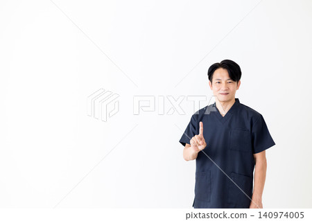 一位身穿藏藍色手術服的中年男醫生舉起他的食指。 一位身穿藏藍色手術服的中年男醫生舉起他的食指。 140974005