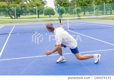 Senior male tennis player crouches down, chasing the ball. Senior male tennis player crouches down, chasing the ball. 140974155