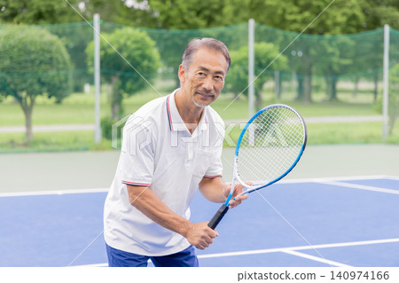 A smiling senior man holding a tennis racket on a tennis court. 140974166