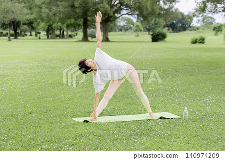 一位微笑、精神矍鑠的老婦人在公園裡做瑜珈三角式。 一位微笑、精神矍鑠的老婦人在公園裡做瑜珈三角式。 140974209