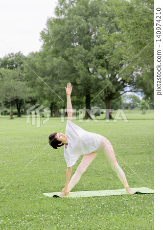 一位微笑、精神矍鑠的老婦人在公園裡做瑜珈三角式。 一位微笑、精神矍鑠的老婦人在公園裡做瑜珈三角式。 140974210