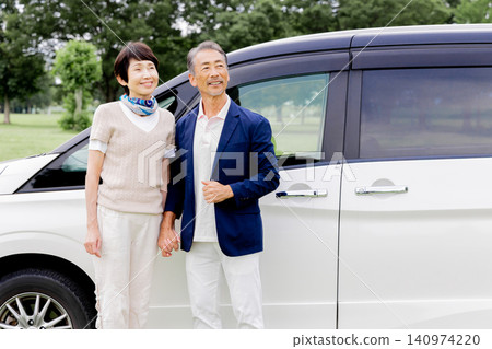 An active senior couple smiles in front of a minivan. An active senior couple smiles in front of a minivan. 140974220