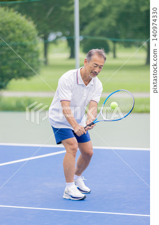 一位老年男子在戶外網球場上反手擊球。 140974330