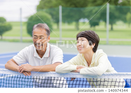 一對老年夫婦在網球場上休息時放鬆微笑。 一對老年夫婦在網球場上休息時放鬆微笑。 140974344