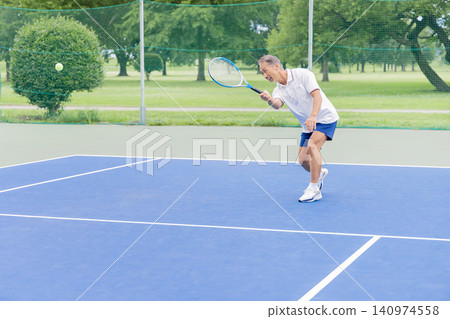 Senior men hitting shots on an outdoor tennis court. 140974558