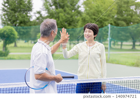 Senior couple high-five each other after winning a doubles tennis match. Senior couple high-five each other after winning a doubles tennis match. 140974721