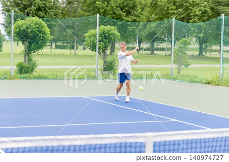 A senior man hitting a forehand on a tennis court. 140974727