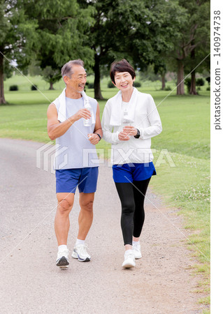 A smiling, active senior couple enjoying a walk and staying hydrated. 140974738