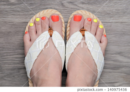 Top view of woman feet in white flip flops with colorful neon pedicure on wooden floor Top view of woman feet in white flip flops with colorful neon pedicure on wooden floor 140975436