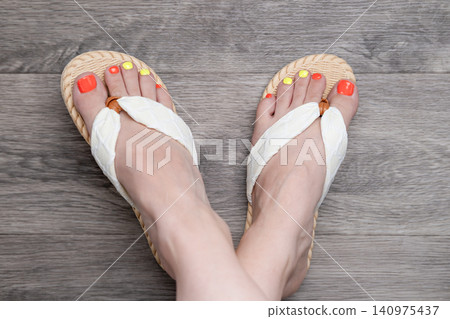 Top view of crossed female feet wearing white flip flops with bright neon pedicure Top view of crossed female feet wearing white flip flops with bright neon pedicure 140975437