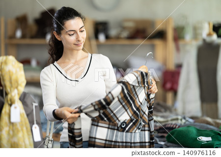 Young woman chooses plaid coat in clothing store Young woman chooses plaid coat in clothing store 140976116