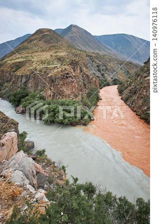 Two mountain rivers merging, one muddy red and one gray. Natural phenomenon where two distinct colored waters meet and flow side by side. Two mountain rivers merging, one muddy red and one gray. Natural phenomenon where two distinct colored waters meet and flow side by side. 140976118