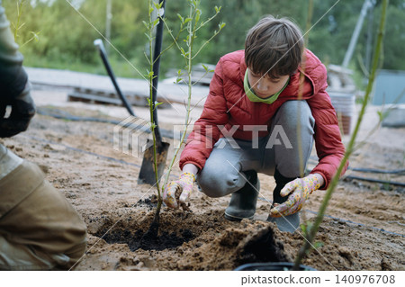 A teenage boy plants a dogwood shrub on their countryside property A teenage boy plants a dogwood shrub on their countryside property 140976708