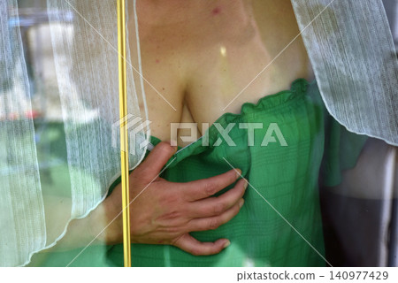 Female portrait of a woman wearing a green dress, standing indoors near a window with curtains, illuminated by soft natural light creating a gentle and elegant atmosphere. Female portrait of a woman wearing a green dress, standing indoors near a window with curtains, illuminated by soft natural light creating a gentle and elegant atmosphere. 140977429