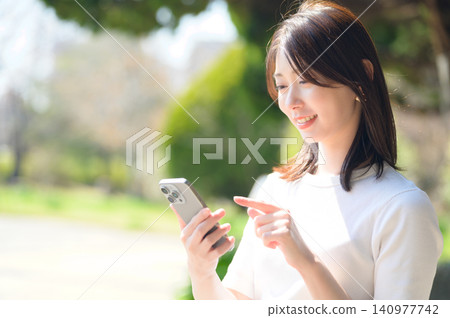 Japanese woman using her smartphone in a park 140977742