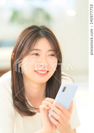 一名日本女子躺在地板上,手裡拿著智慧型手機 一名日本女子躺在地板上,手裡拿著智慧型手機 140977758