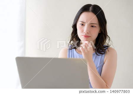 A Japanese woman pondering while looking at her laptop. A Japanese woman pondering while looking at her laptop. 140977803
