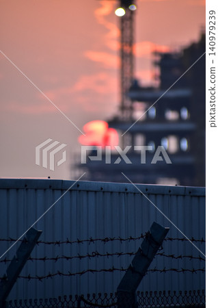 Close-up of metal corrugated board with sunset background and construction site. Fence from corrugated board. Texture of metal fence. For background use. Close-up of metal corrugated board with sunset background and construction site. Fence from corrugated board. Texture of metal fence. For background use. 140979239