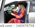 Driver blonde woman sits in gray car and holds steering wheel while looking forward with tense expression. Horizontal. 140979758