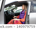 Driver woman blonde sits inside car parked outdoors. She holds steering wheel while looking forward. Horizontal. 140979759