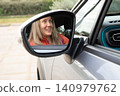 Driver woman sits and smiles in car mirror reflection observing surroundings during daylight. Horizontal. Selective focus. 140979762