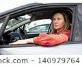 Driver woman with blonde hair sits inside car in parking lot. She looks outside with a focused expression. Horizontal. Close-up. 140979764