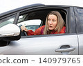 Driver blonde woman looks surprised in car looking outside in parking lot during daytime. Horizontal. 140979765
