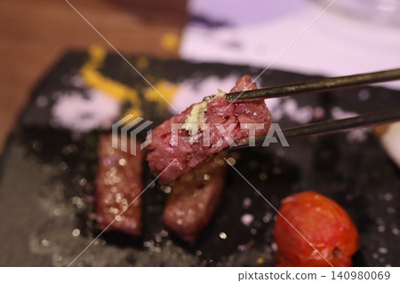 Close-up of Tongs Holding Raw Beef with Garlic Over Slate Plate Close-up of Tongs Holding Raw Beef with Garlic Over Slate Plate 140980069